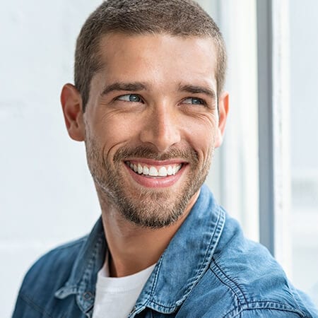 A young man with a beard smiling and wearing a denim jacket