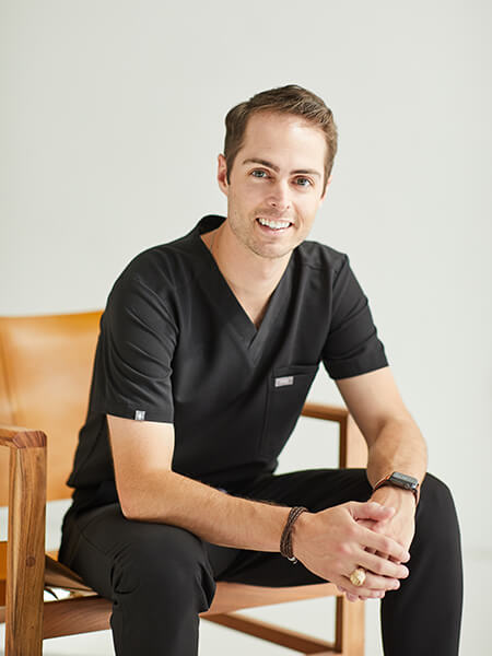 Dr. Ryan Schmidgall sitting in a chair while smiling and wearing a black suit